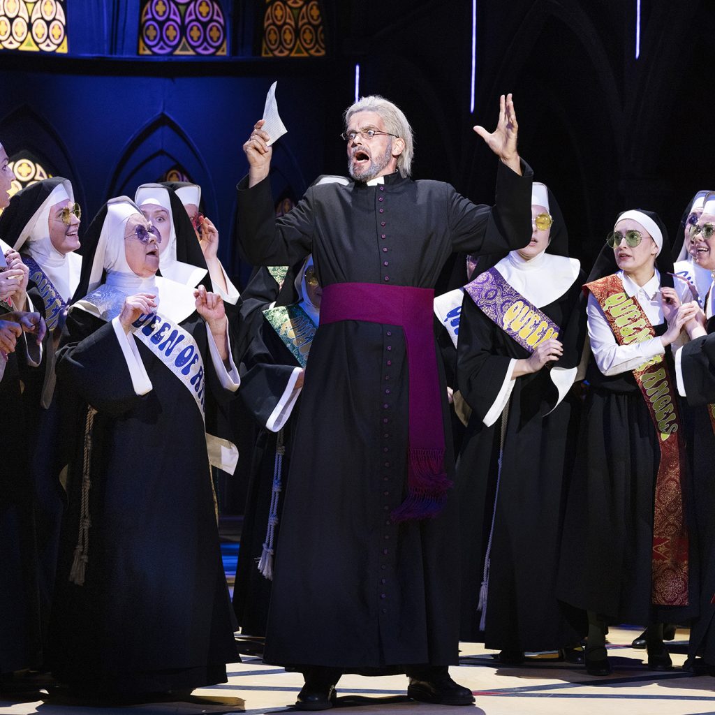 Billede fra 'Sister Act' på Det Ny Teater med skuespilleren Tomas Ambt Kofod i rollen som Biskop O'Hara og Nonnerne i en betagende scene fra forestillingen.