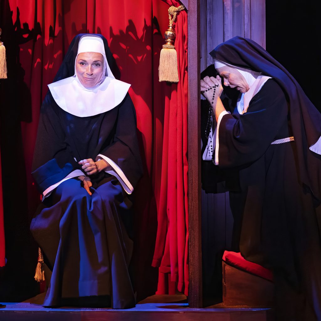 Billede fra 'Sister Act' på Det Ny Teater med skuespillerne Julie Steincke som Deloris og Marianne Mortensen som Abbedissen i en tankevækkende scene i skriftestolen.